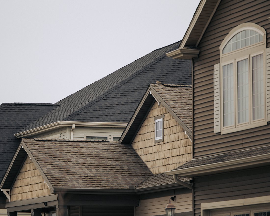 Neighbouring houses with dark and brown architectural shingle roofs, gables and white gutters